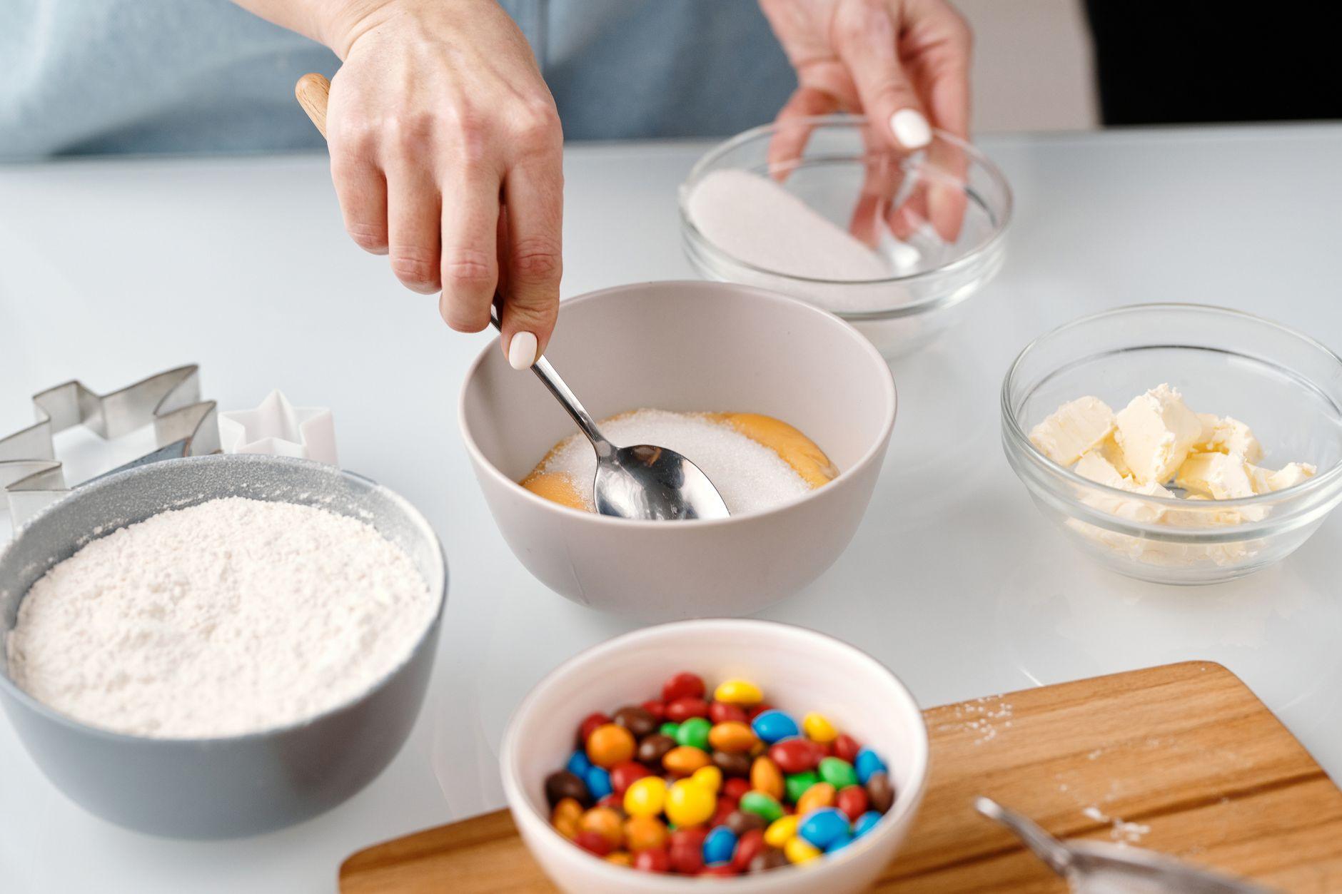 A close-up of white granulated sugar being poured into a glass bowl, representing added sugar in food.