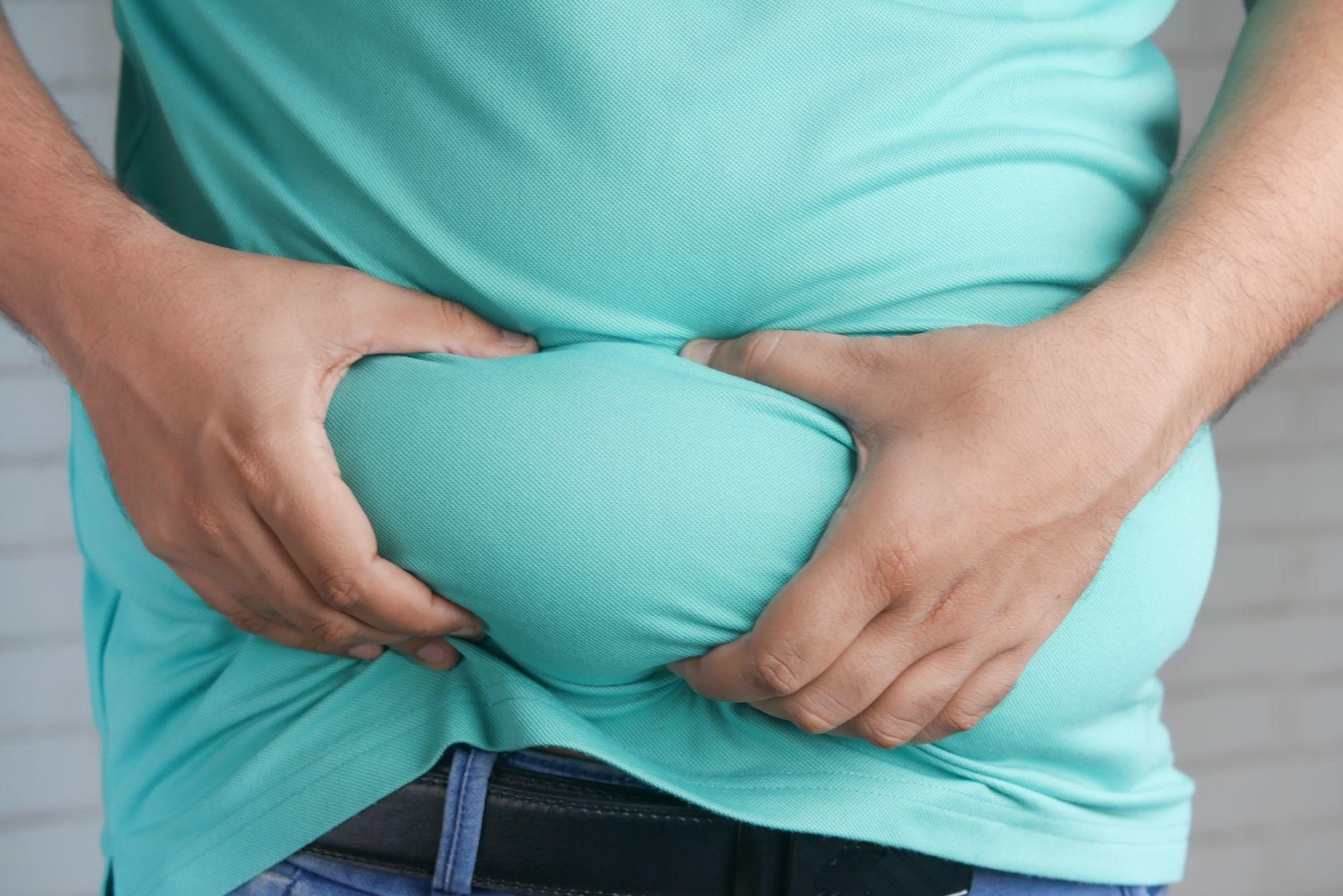 A stressed person holding their abdomen, illustrating the link between high cortisol levels and stubborn belly fat.