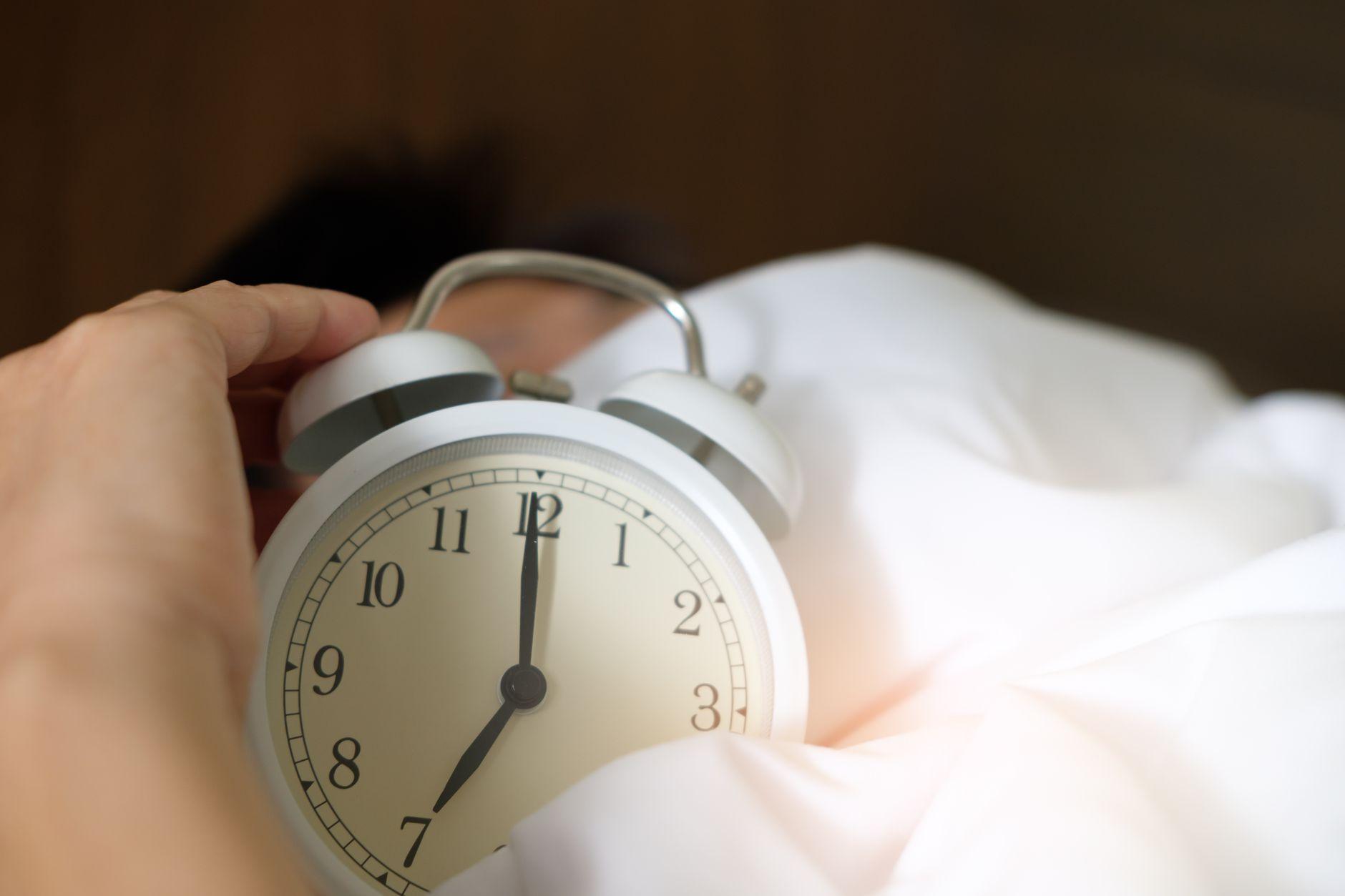 A person looking exhausted while waking up in a dimly lit bedroom, representing the cycle of waking up tired.