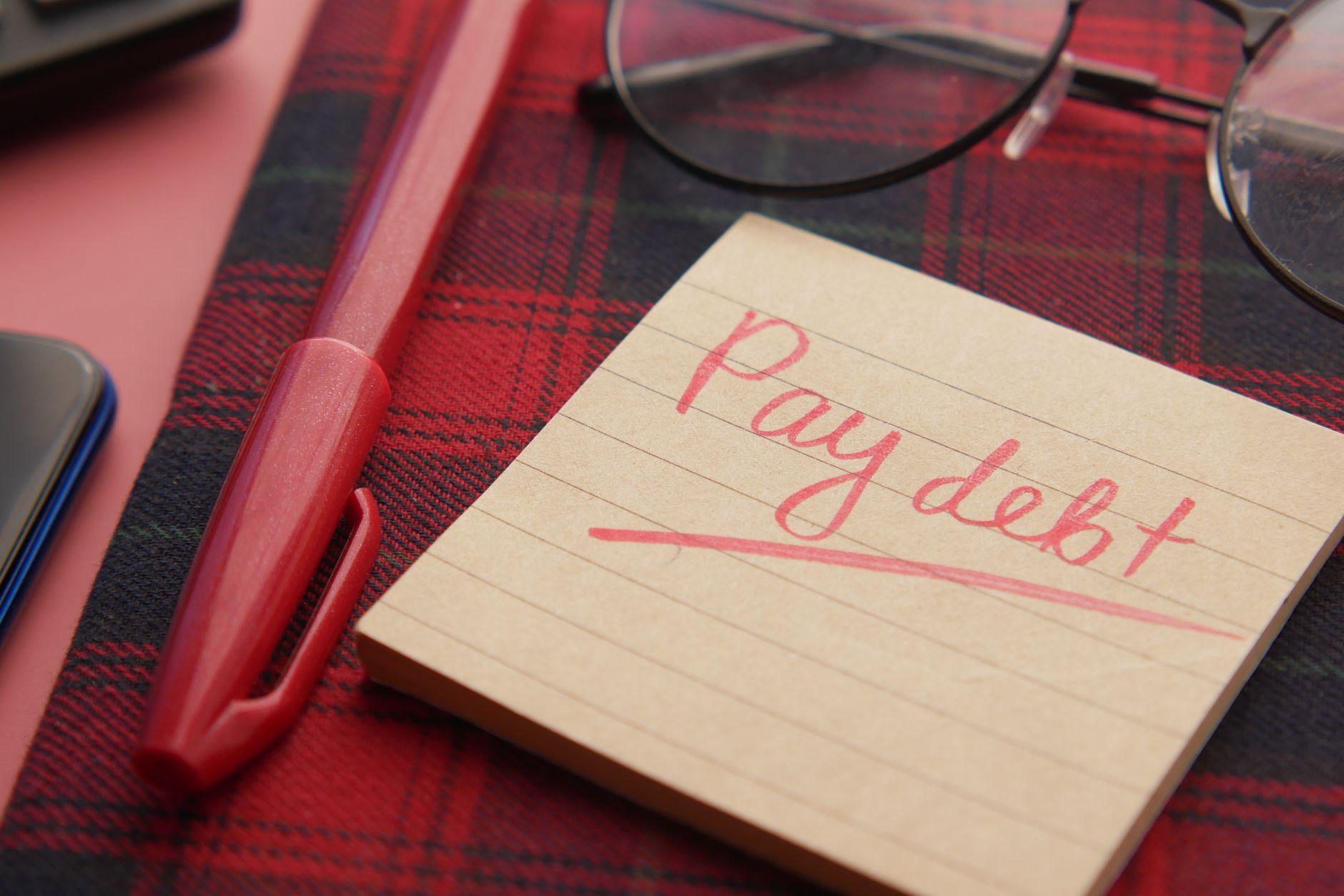 A person holding a calculator with a checklist, representing a strategy for paying off debt.