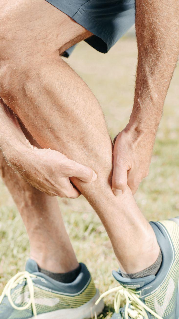 A person sitting on a bed in pain while holding their calf, illustrating nocturnal leg cramps.
